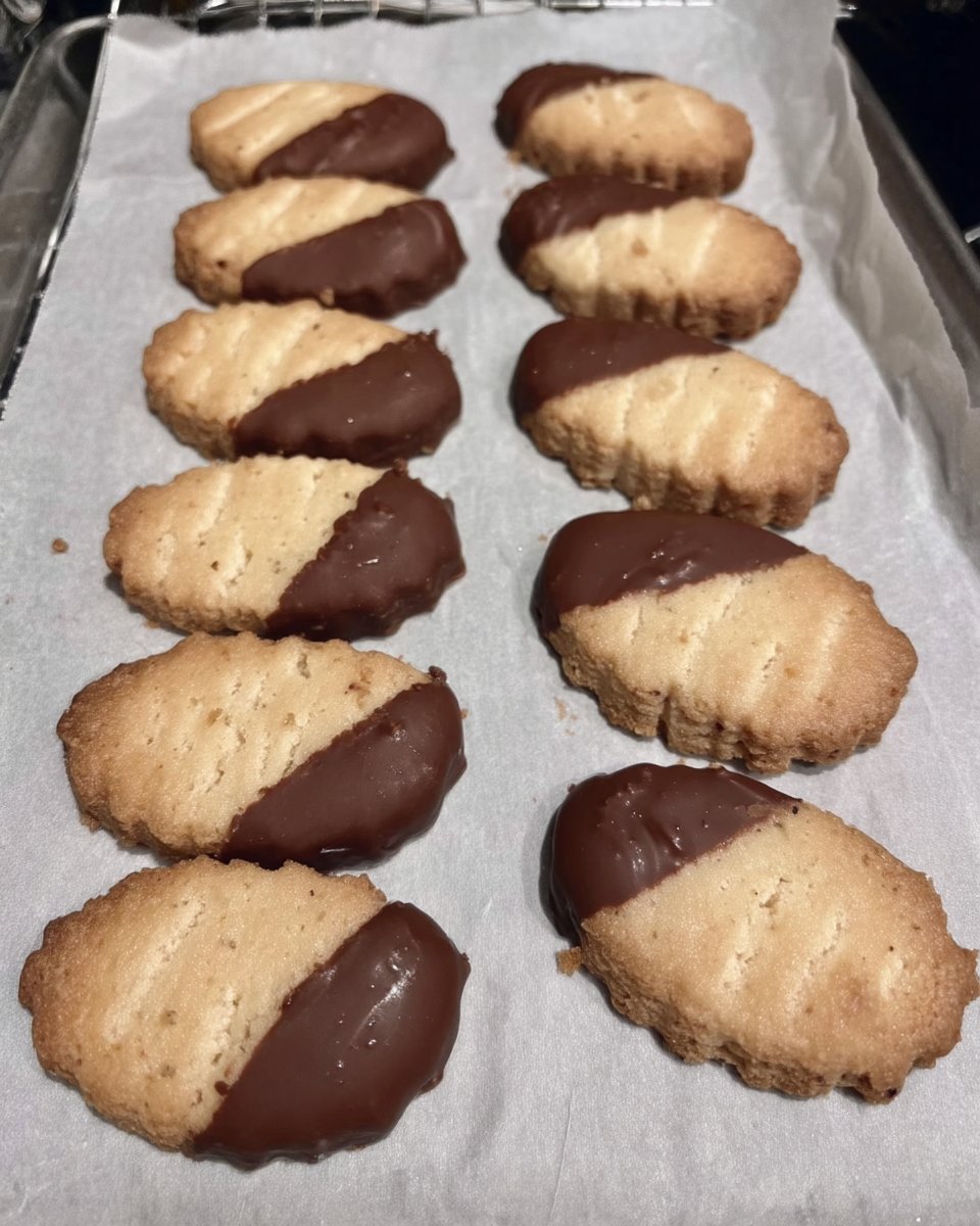 Dipped shortbread cookies on a cooling rack half coated in dark chocolate